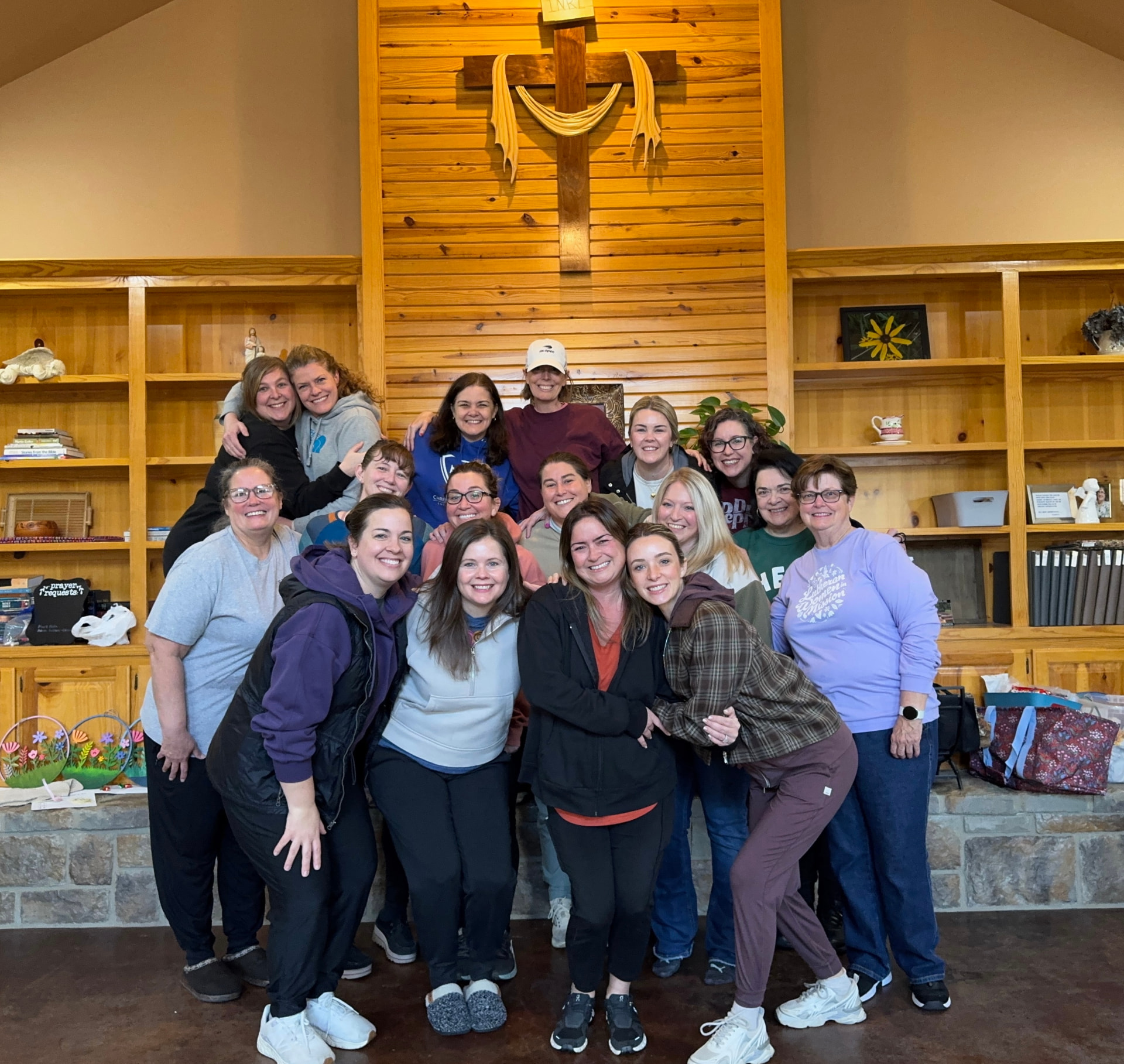 Women smiling together beneath a wooden cross at the CTR women's retreat