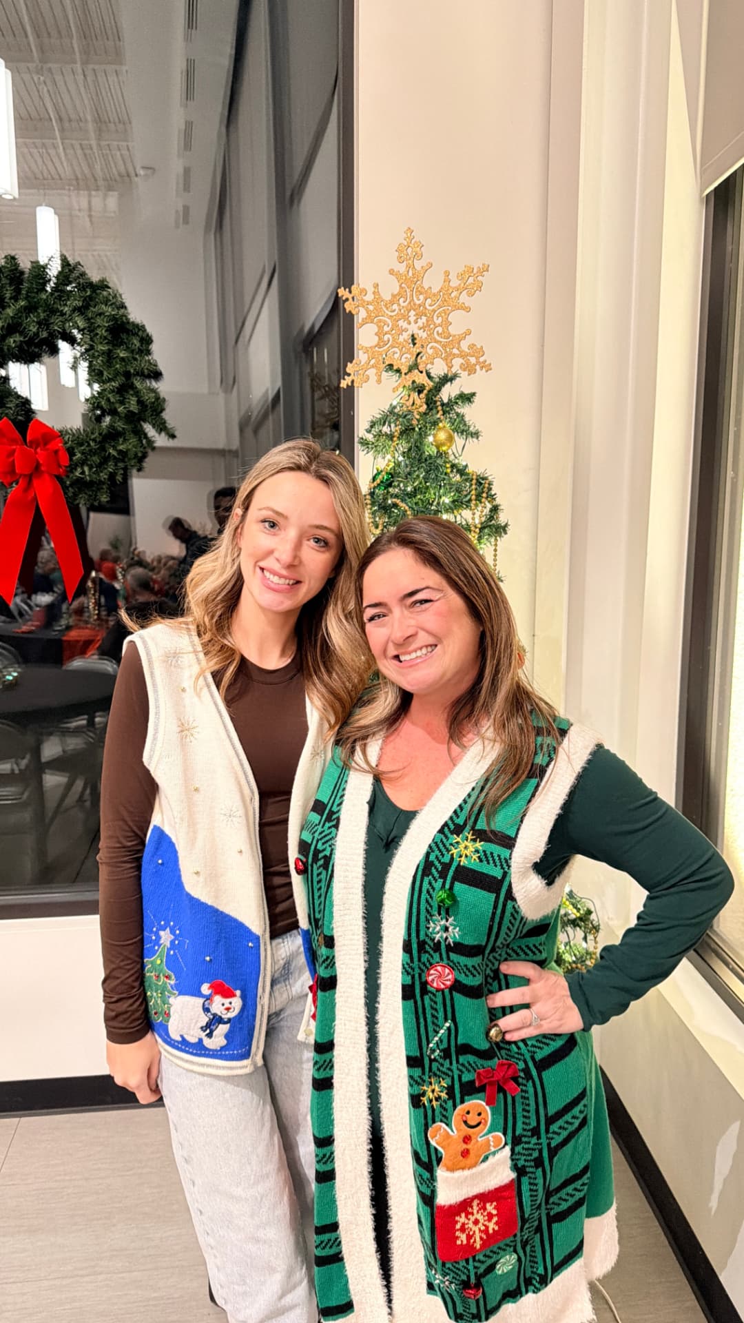 Two members posing in festive Christmas sweaters by a Christmas tree